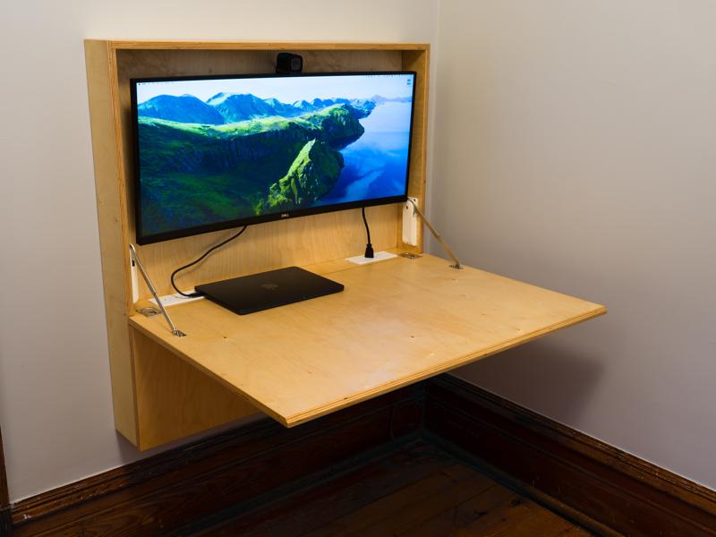 A convertible, fold-down desk. It is currently open with the desk folded down and a compute hooked up to the display. Made from baltic birch.